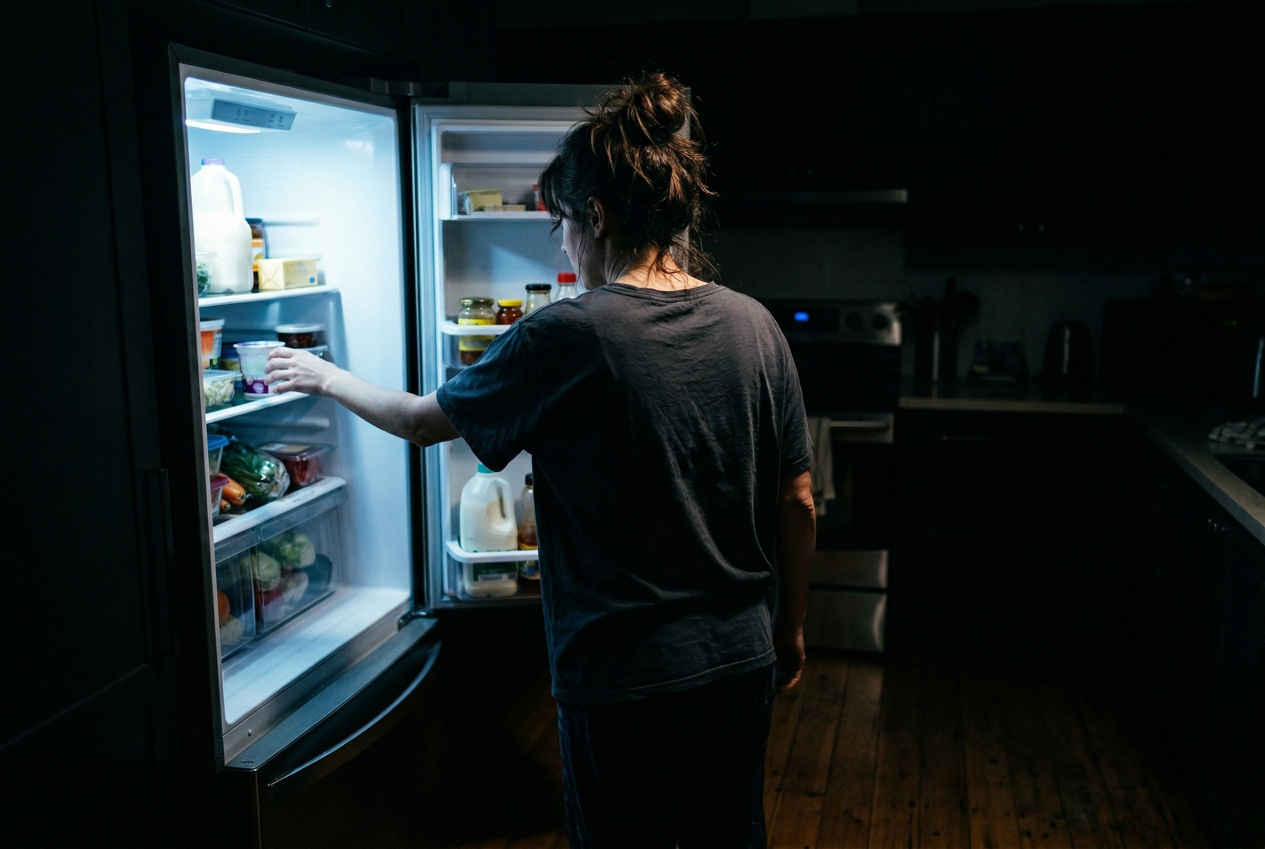 A woman standing alone in a dimly lit kitchen at night